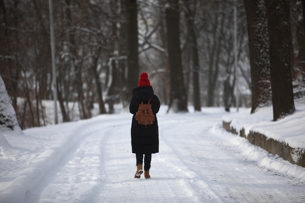 Mujer en traje de invierno caminando por la carretera nevada del parque