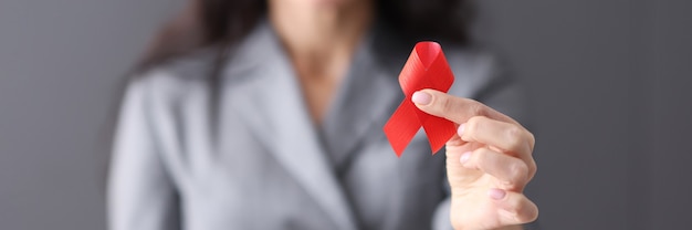 Mujer en traje de negocios sosteniendo una cinta roja en sus manos closeup concepto del día mundial del sida
