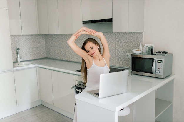 Mujer con traje negro sonriendo al portátil en la cocina