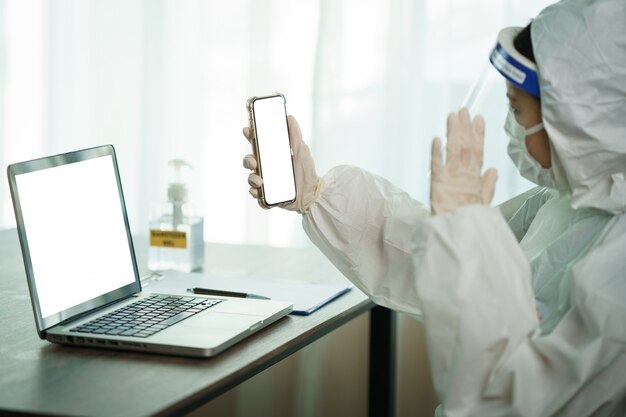 Mujer en traje protector de materiales peligrosos trabajador en computadora de laboratorio descansando y videollamadas en teléfonos inteligentes. para detener la propagación del coronavirus o COVID-19.