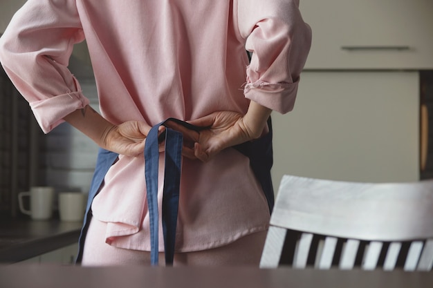 Mujer en traje rosa corbatas delantal azul en la espalda para comenzar a cocinar en la cocina de su casa imagen sin rostro