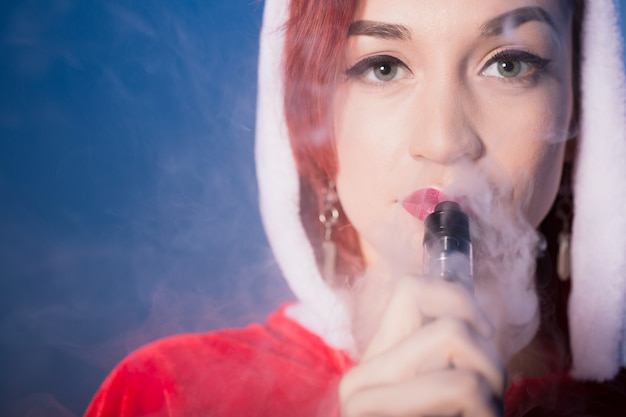 Mujer en traje de santa fumando cigarrillo electrónico y exhalando humo