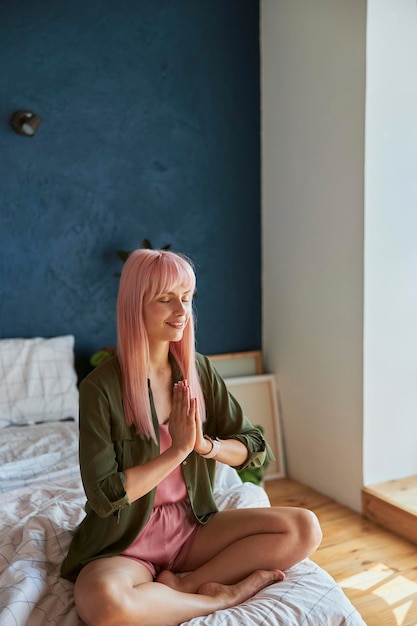 Mujer tranquila con cabello largo rosa medita sosteniendo la mano pecado namaste en cama grande