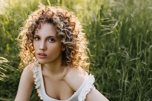 Mujer tranquila joven con pelo rizado sentado en un campo con hierba verde