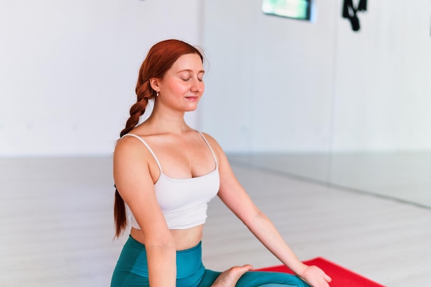 Mujer tranquila con los ojos cerrados y las manos de loto practica el ejercicio de yoga en la alfombra en la clase de estudio