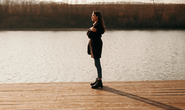 Mujer tranquila de pie en el muelle cerca del lago al atardecer