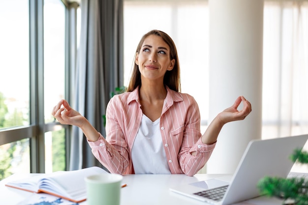 Mujer tranquila que se relaja meditando con una computadora portátil sin alivio libre de estrés en el concepto de trabajo consciente y pacífica joven mujer de negocios o estudiante practicando ejercicios de yoga de respiración en la meditación de la oficina en el lugar de trabajo