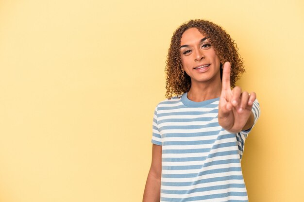 Mujer transexual latina joven aislada sobre fondo amarillo que muestra el número uno con el dedo.