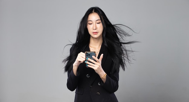 Mujer transgénero asiática con pelo largo y negro y liso, tiro de viento en el aire Mujer sostenga el teléfono contra la tormenta de viento sintiendo moda sensual sexy fondo gris aislado copia espacio