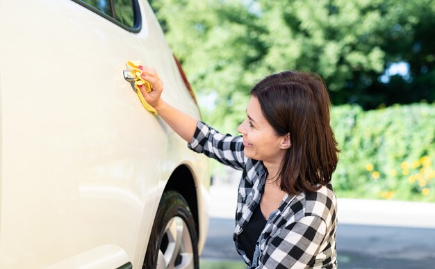 Mujer con trapo de microfibra para limpiar el coche en el fondo de la naturaleza