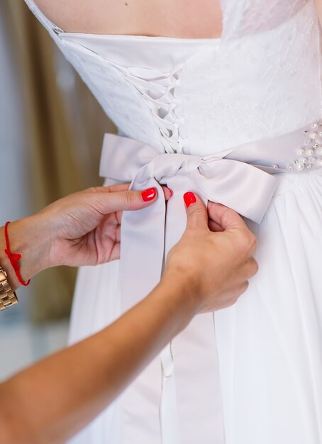 Mujer tratando de vestido de novia en una tienda con ayudante de mujeres.