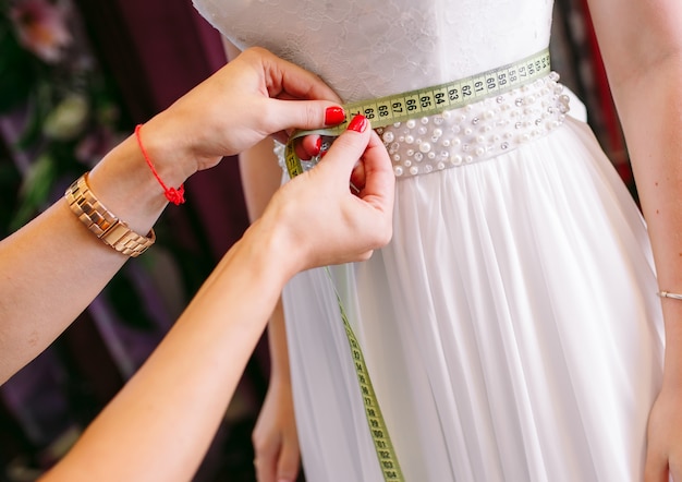 Mujer tratando de vestido de novia en una tienda con ayudante de mujeres.