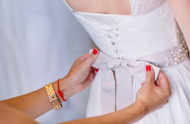 Mujer tratando de vestido de novia en una tienda con ayudante de mujeres.