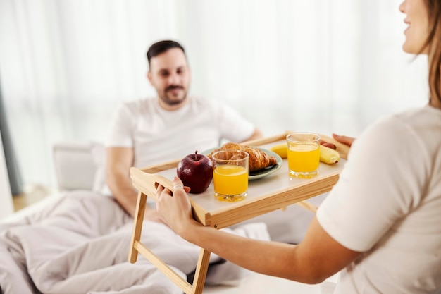 Una mujer trayendo el desayuno en la cama para su esposo en su dormitorio.