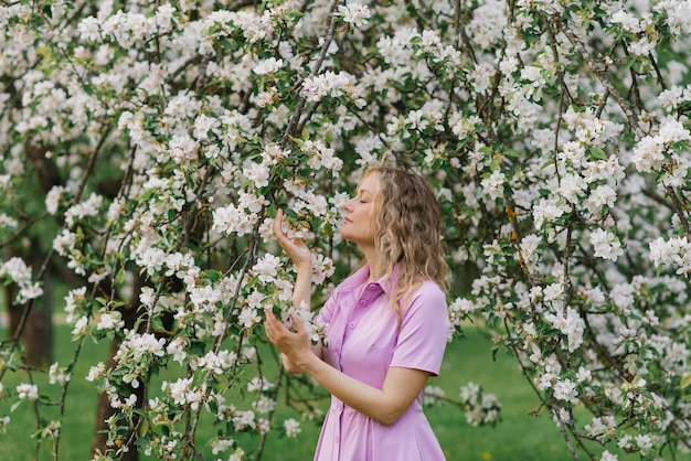 Una mujer de treinta años huele una rama de un árbol en flor en el parque en primavera