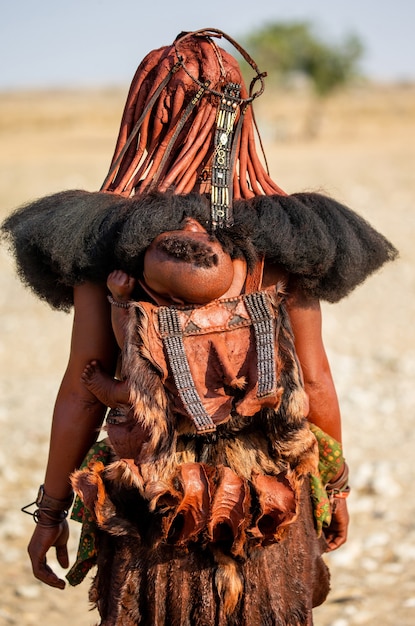 Mujer de la tribu Himba con un niño a sus espaldas en traje tradicional.