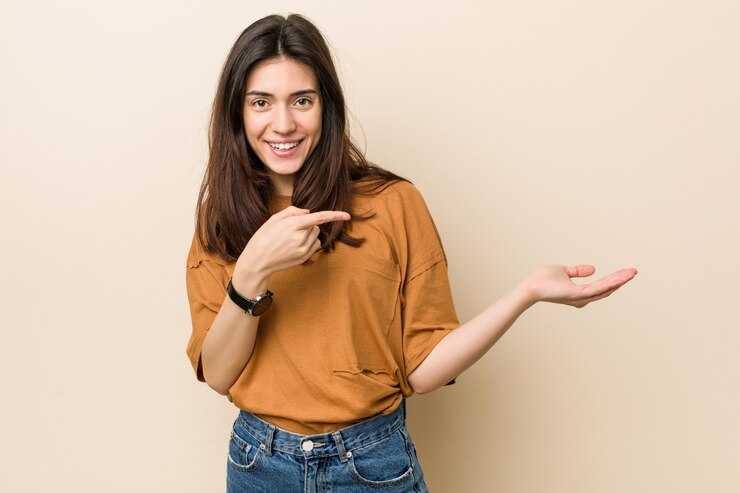 Foto la mujer triguena joven contra un fondo beige excitó sostener un espacio de la copia en la palma.