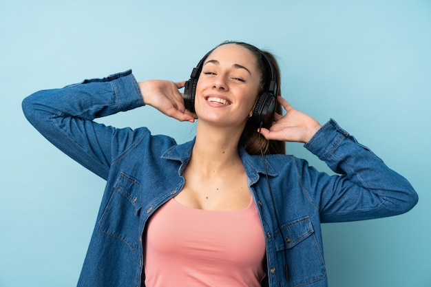 Mujer triguena joven sobre música que escucha aislada de la pared azul