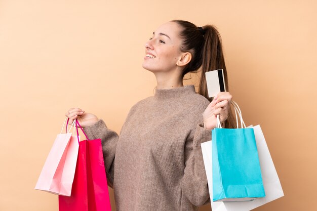 Mujer triguena joven sobre la pared aislada que sostiene bolsos de compras y una tarjeta de crédito