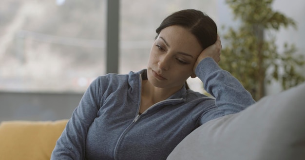 Una mujer triste y agotada sentada en el sofá de su casa se siente sola y sin esperanza por el concepto de trastorno mental