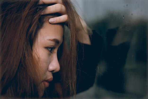 Mujer triste asiática de primer plano en el espejo con reflejo en un día de lluvia concepto de mujer de angustia de estilo vintage niña