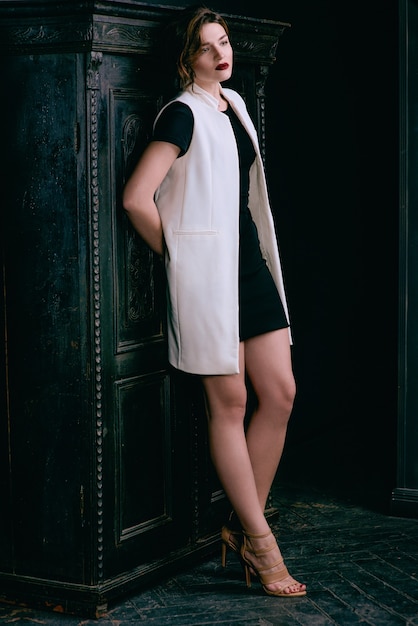 Mujer triste con cabello castaño corto con elegante maquillaje en vestido negro y chaleco blanco