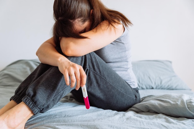 Mujer triste en la cama con prueba de embarazo negativa