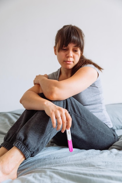 Mujer triste en la cama con prueba de embarazo negativa