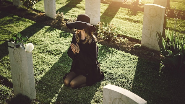 Mujer triste en el cementerio rezando en la lápida