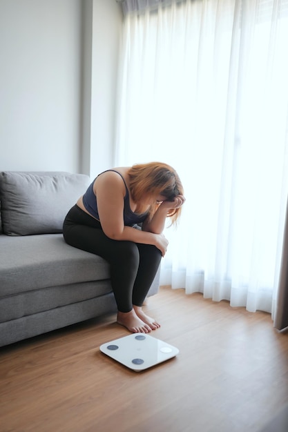 Mujer triste con grasa molesta aburrida de hacer dieta pérdida de peso fracasa dieta grasa y escala mujer asiática triste en la escala de peso en el control de peso en casa