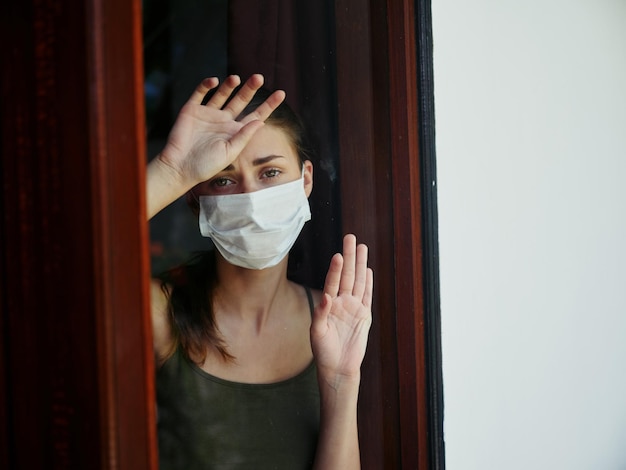 Mujer triste con máscara médica mirando por la ventana foto de alta calidad