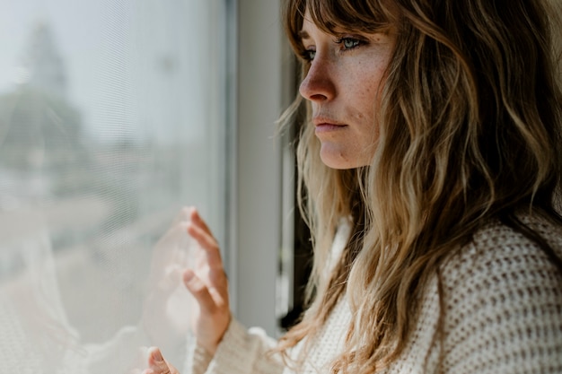 Mujer triste mirando por la ventana durante un encierro