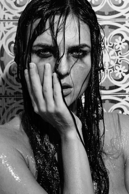 Mujer triste y mojada con maquillaje manchado en la cara bajo la ducha