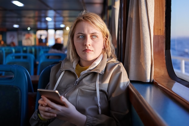 Mujer triste pasajero del ferry con teléfono móvil en sus manos mira por la ventana