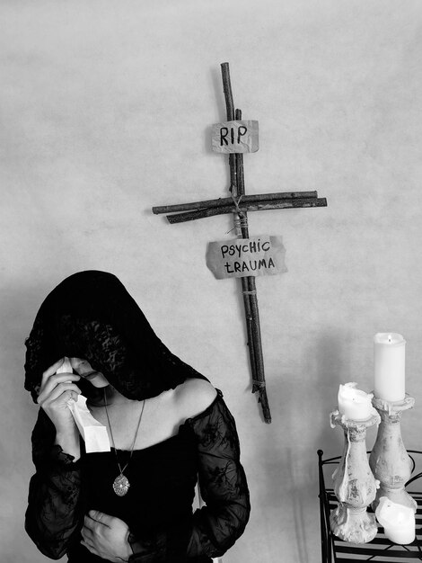 Foto mujer triste de pie con cruz y texto colgado en la pared