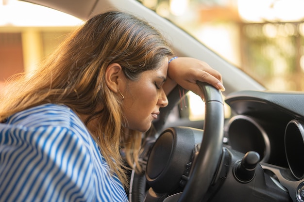 Foto mujer triste porque se estrelló mientras conducía apoyando su cabeza en el volante