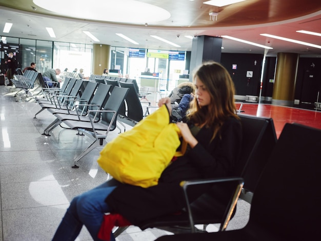 Foto mujer triste sentada en el aeropuerto con una mochila amarilla esperando foto de alta calidad