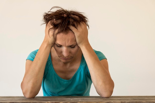 Foto mujer triste sentada en la mesa contra la pared