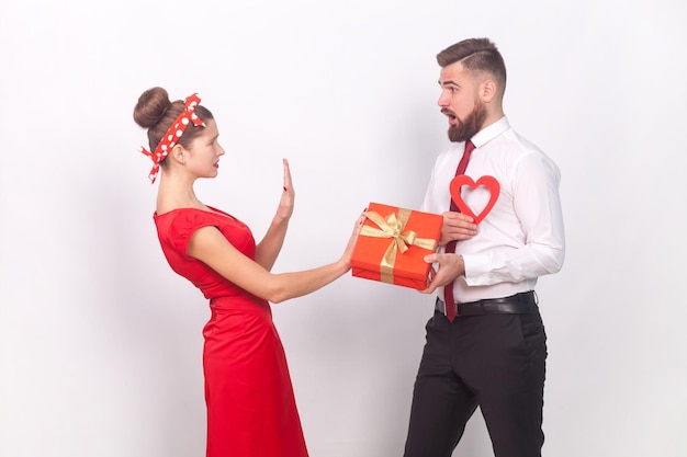 Mujer triste sorprendida que muestra un gesto de parada al hombre con el presente y una mujer de corazón que dice que no rechace un regalo