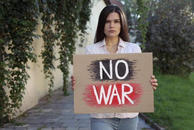 Mujer triste sosteniendo un cartel con palabras No War al aire libre Espacio para texto