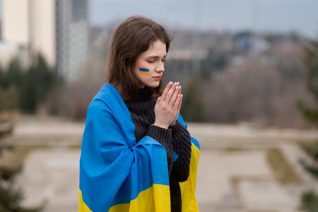 Mujer triste de tiro medio rezando con la bandera ucraniana