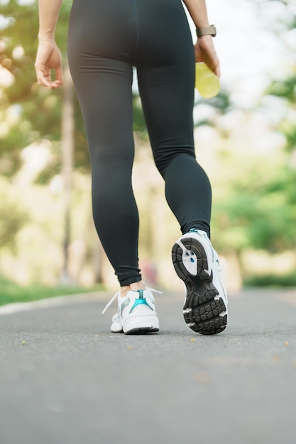 Mujer trotando y caminando en la carretera por la mañana Hembra adulta joven en zapatos deportivos corriendo en el parque fuera de los músculos de las piernas del atleta Ejercicio bienestar estilo de vida saludable y conceptos de entrenamiento