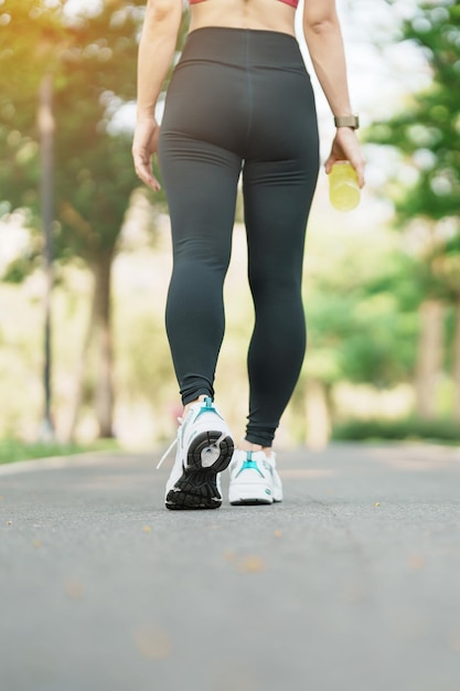 Mujer trotando y caminando en la carretera por la mañana Hembra adulta joven en zapatos deportivos corriendo en el parque fuera de los músculos de las piernas del atleta Ejercicio bienestar estilo de vida saludable y conceptos de entrenamiento