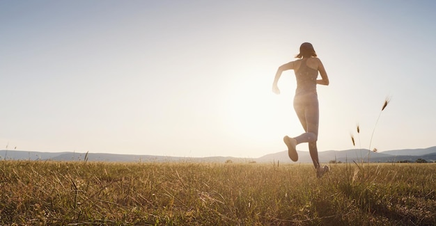 Mujer trotando corriendo en el campo de verano al atardecer