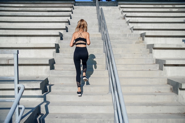 Mujer trotar entrenamiento concepto de bienestar. Estilo de vida saludable, gimnasio deportivo niña corriendo por las escaleras de piedra.