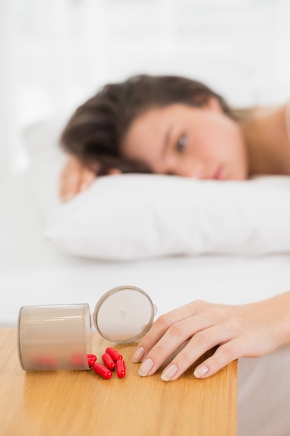 Foto mujer tumbada en la cama por la botella derramada de pastillas en la mesa