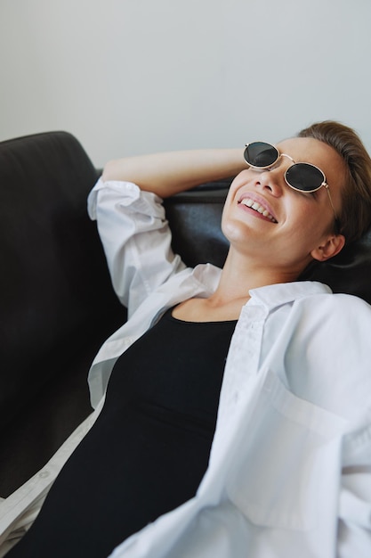 Una mujer tumbada en el sofá con las gafas puestas y retorciéndose