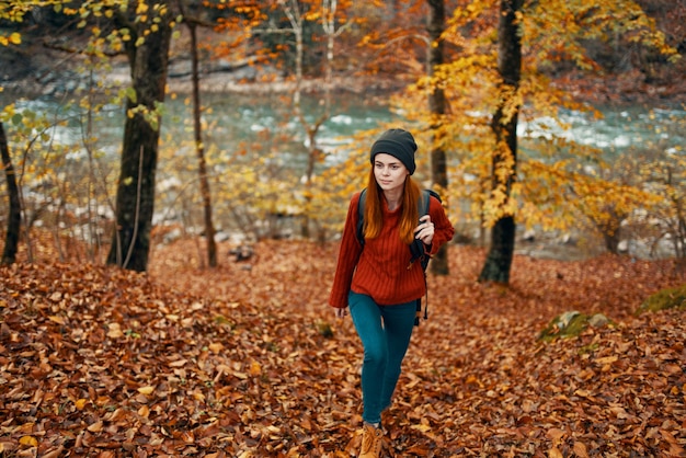 Mujer de turismo de viajes en suéter y jeans en el bosque de otoño cerca del río de la montaña