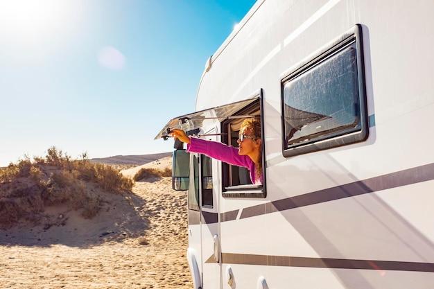 Mujer turista adulta abriendo la ventana de la autocaravana para disfrutar del sol y la libertad. Concepto de personas de viaje para vacaciones de verano dentro de un vehículo de autocaravana de autocaravana. Estilo de vida nómada de la libertad