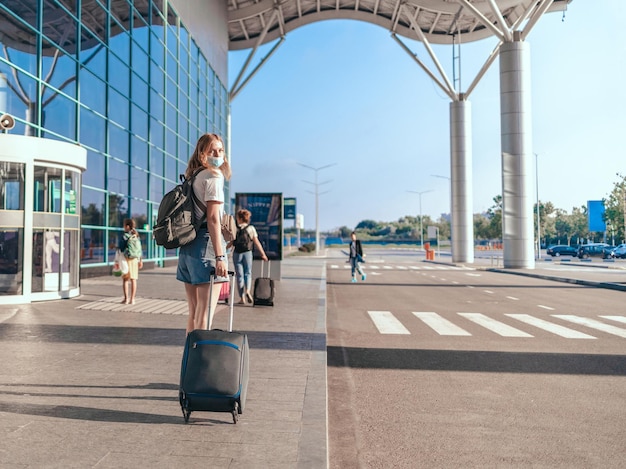 Mujer turista del aeropuerto de viaje COVID-19 con mochila y maleta de equipaje de mano parada cerca de la terminal del aeropuerto internacional esperando el embarque. Concepto de estilo de vida activo